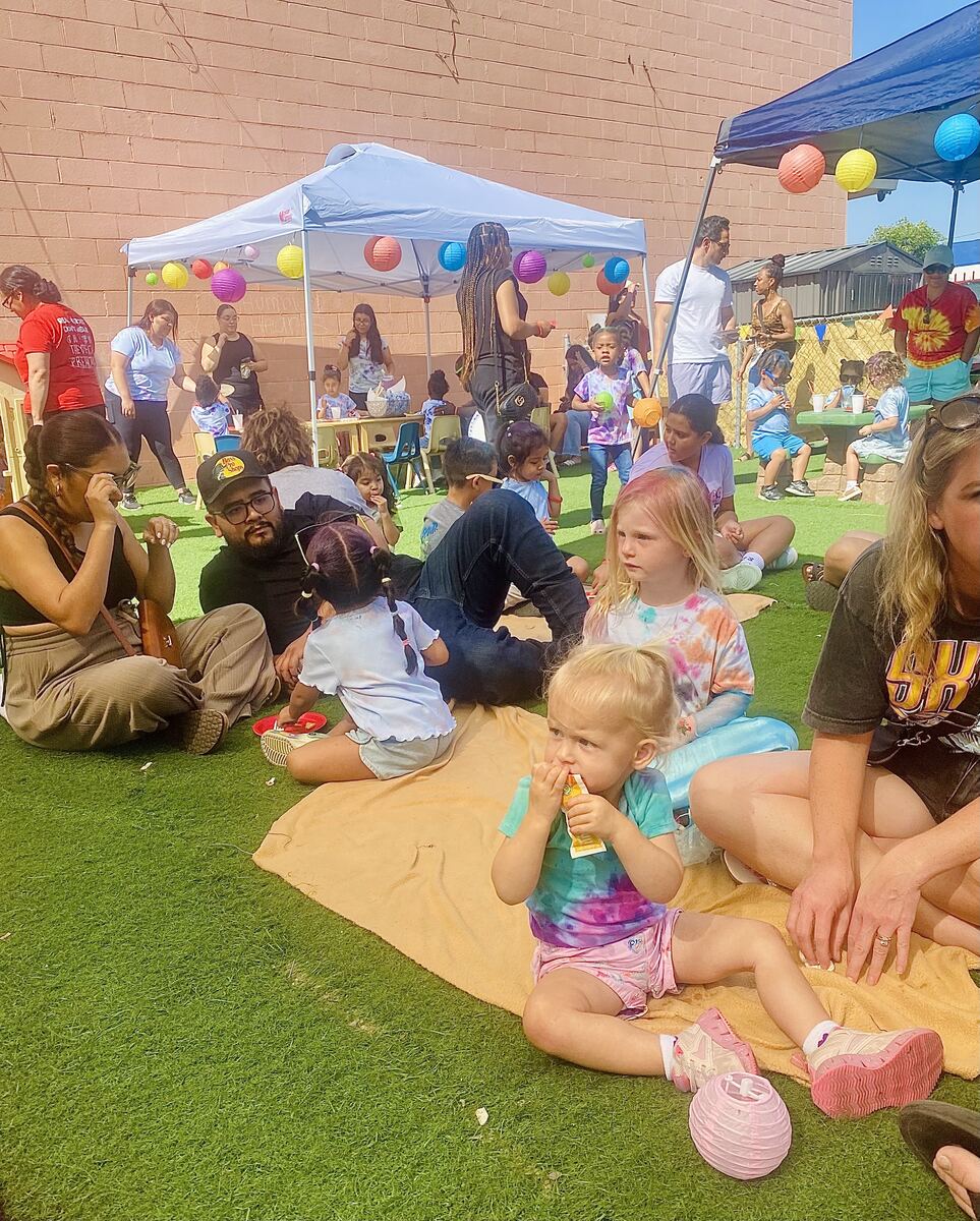 Families and children gathered on the turf under a canopy at a school community event