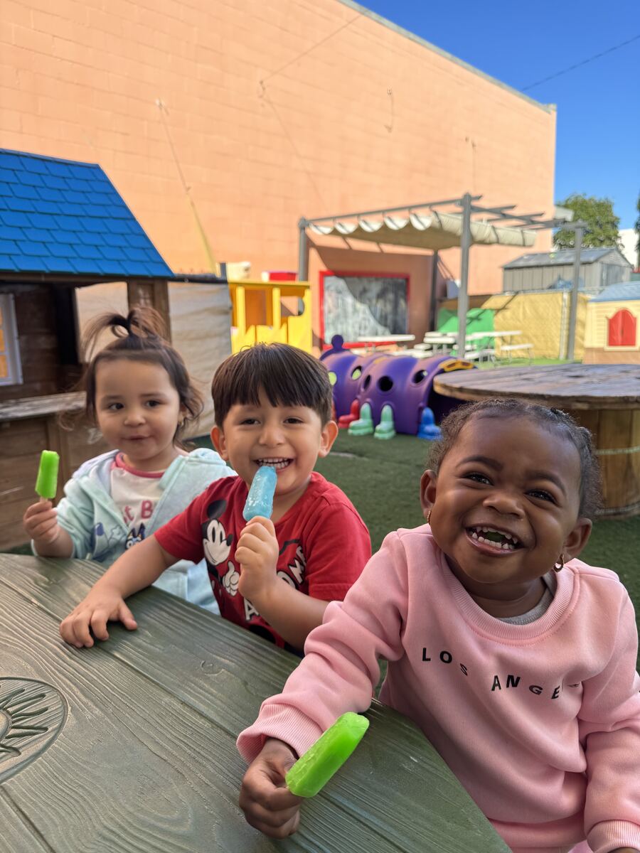 Three smiling toddlers at an outdoor picnic table enjoying fruit popsicles