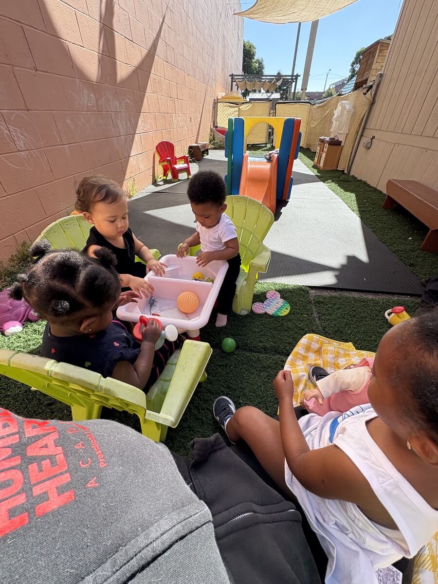 Toddlers playing together at a water table in the shaded outdoor play yard
