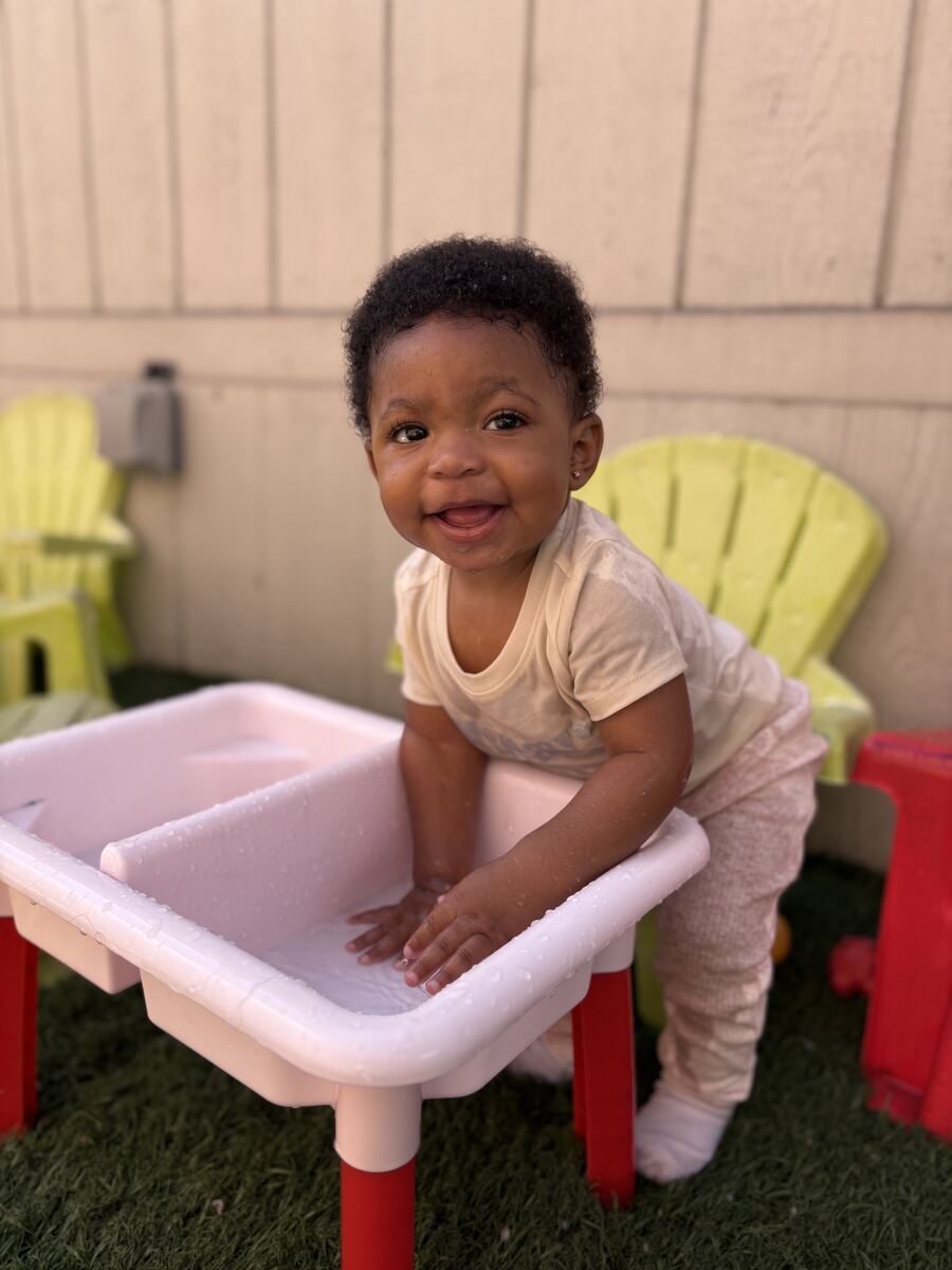 Smiling baby standing at a water table in the outdoor play yard