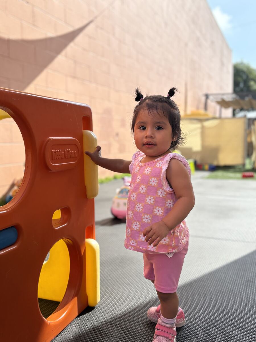 Toddler in a pink floral top standing next to the play structure on the playground